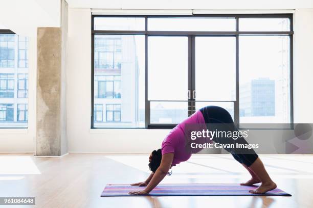 side view of woman practicing downward facing dog position yoga against window - downward facing dog position stock pictures, royalty-free photos & images