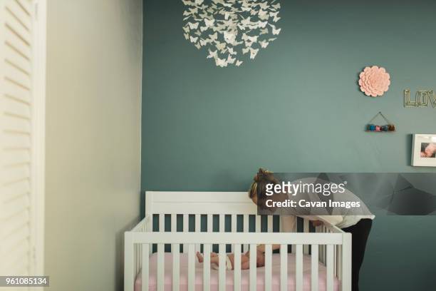 mother looking at newborn daughter lying in crib against wall - slaapkamer zijaanzicht stockfoto's en -beelden