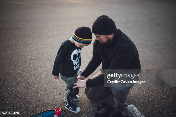 father assisting son in wearing kneepad on field - knieschützer stock-fotos und bilder