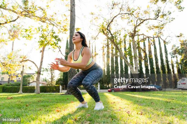 woman practicing jump squats in park - hockend stock-fotos und bilder