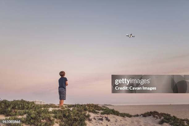 rear view of boy looking quadcopter while standing at beach against sky - only kids at sky stockfoto's en -beelden