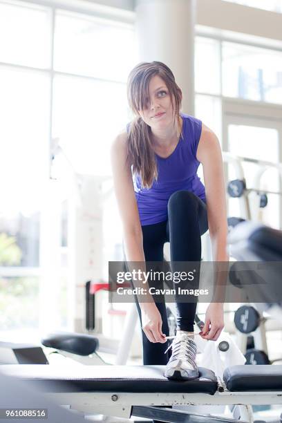 young woman looking away while tying shoelace in gym - lace fastener stock pictures, royalty-free photos & images