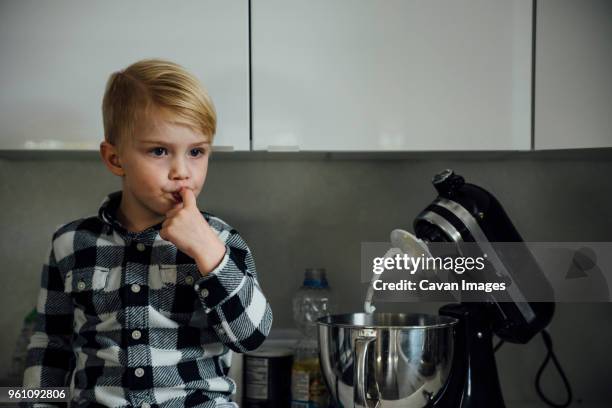 cute boy tasting food from mixer in kitchen - finger in mouth fotografías e imágenes de stock