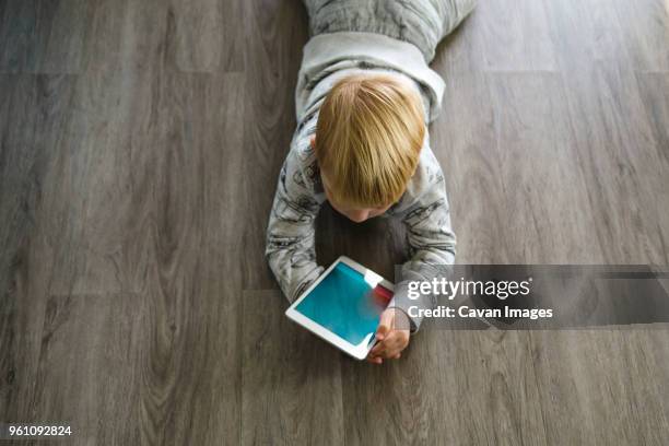 high angle view of boy using tablet computer while lying on floor at home - auf rücken liegen stock-fotos und bilder