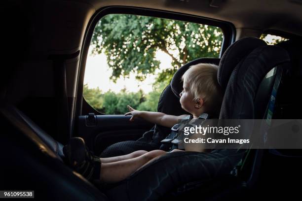 shirtless baby boy looking through window while sitting in car seat - toddler in car foto e immagini stock