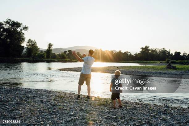 rear view of father with son playing at lakeshore against clear sky during sunset - bismarck north dakota stock pictures, royalty-free photos & images