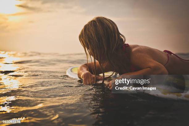 woman lying on surfboard in sea against sky - indonesia surfing stock pictures, royalty-free photos & images