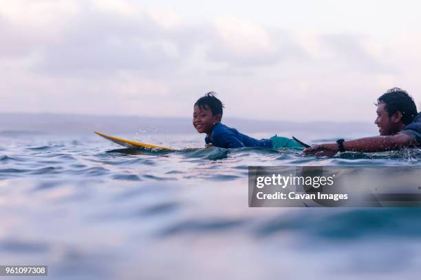 father and son surfing in sea against sky - indonesia surfing stock pictures, royalty-free photos & images