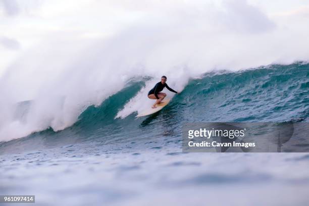 full length of woman surfing in sea - surfer wetsuit stockfoto's en -beelden