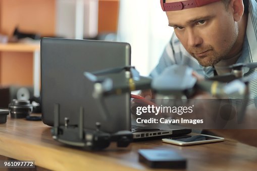 Engineer using mobile phone while examining quadcopter at table in office Engineer using mobile phone while examining quadcopter at table in office