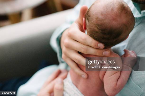 midsection of father carrying newborn daughter while sitting on chair at home - birthing chair stock pictures, royalty-free photos & images