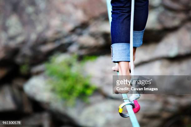 low section of woman walking on rope against rocks - slackline stockfoto's en -beelden