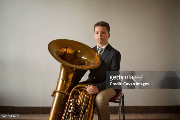 portrait of confident boy with tuba against white wall - tube foto e immagini stock