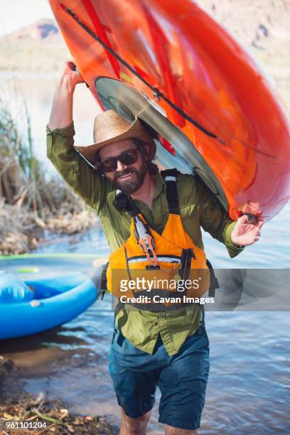 portrait of happy man carrying paddleboard at lakeshore - carrying kayak stock pictures, royalty-free photos & images