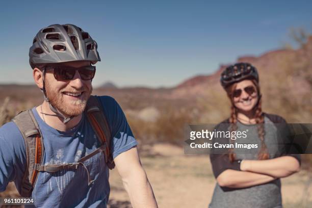 happy male and female mountain bikers standing on mountain against clear blue sky - confidence male landscape stock-fotos und bilder