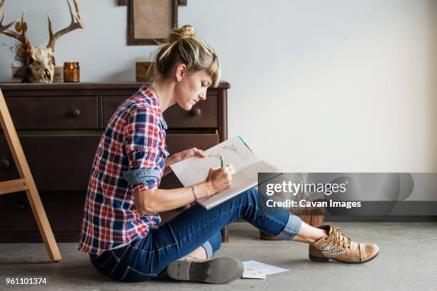 concentrated female artist drawing in book while sitting at home - artist drawing stock-fotos und bilder