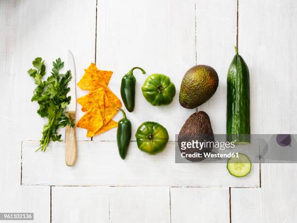 avocados, green tomatoes, jalapeno peppers, cucumber, parsley, kitchen knife and tortilla chips on white wood - slätpersilja bildbanksfoton och bilder