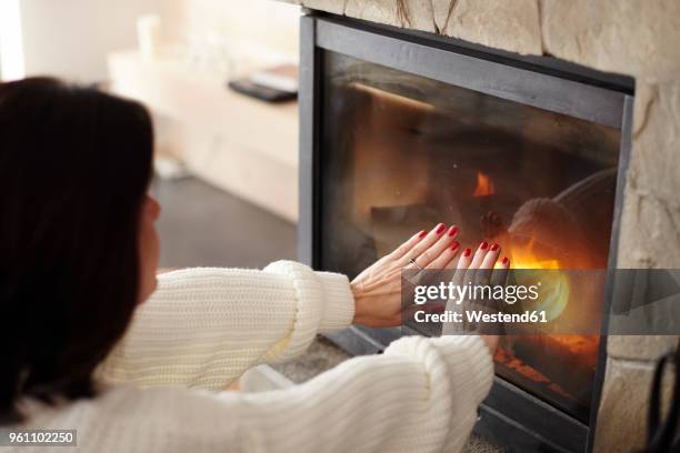mature woman warming her hands at the fireplace - lagerfeuer stock-fotos und bilder