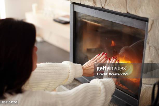 mature woman warming her hands at the fireplace - haardvuur stockfoto's en -beelden