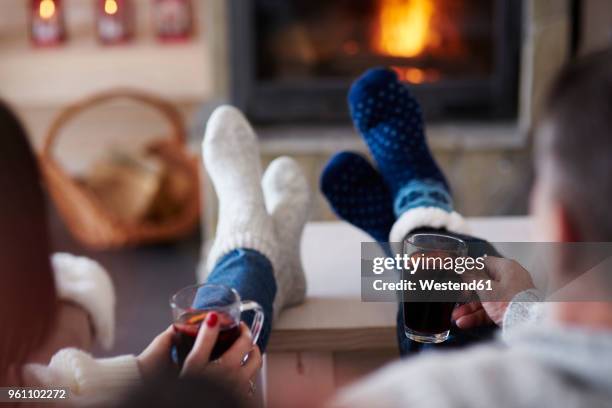 mature couple with hot drinks in living room at the fireplace - haardvuur stockfoto's en -beelden