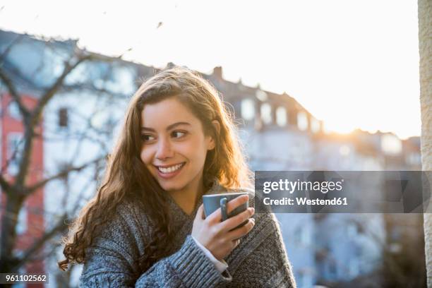 portrait of laughing teenage girl with coffee mug on balcony at twilight - ringellocke stock-fotos und bilder