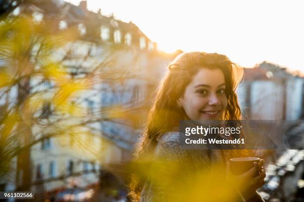 portrait of laughing teenage girl with coffee mug on balcony at twilight - ringellocke stock-fotos und bilder