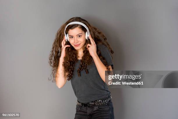 portrait of teenage girl with curly hair listening music with headphones - pijpenkrul stockfoto's en -beelden
