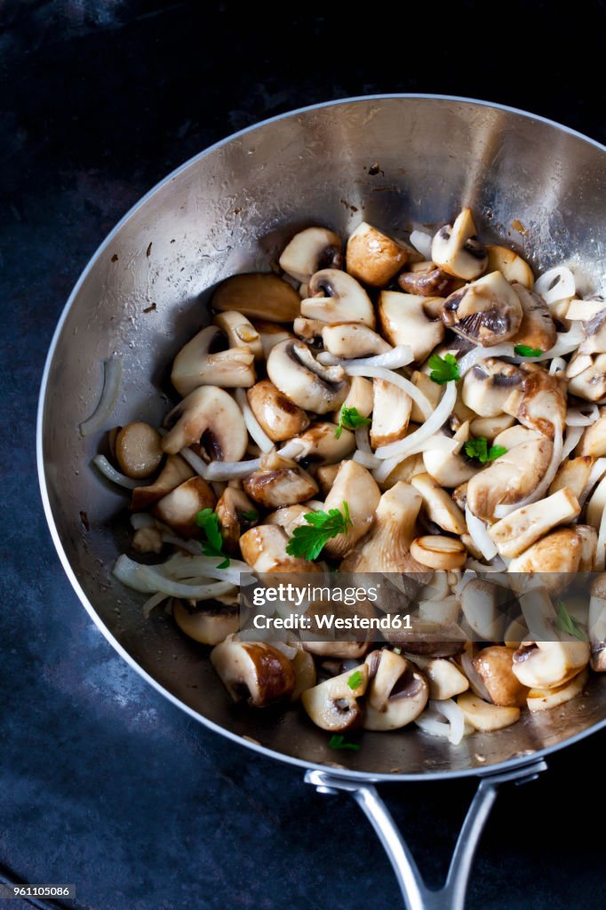 Fried champignons and king trumpet mushrooms with onions and parsley in pan