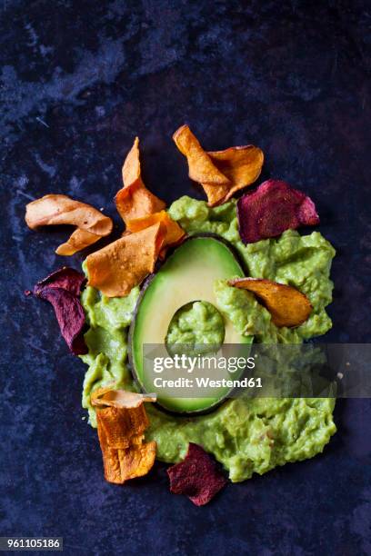guacamole, slice of avocado and vegetable chips on dark ground - vegetable chips stock pictures, royalty-free photos & images