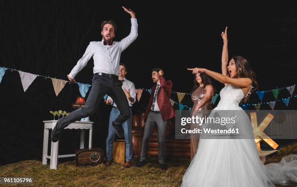 surprised bride looking at man jumping on a night field party with friends - hochzeit stock-fotos und bilder