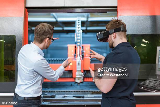 man explaining machine to colleague wearing vr glasses in factory - vr stock-fotos und bilder