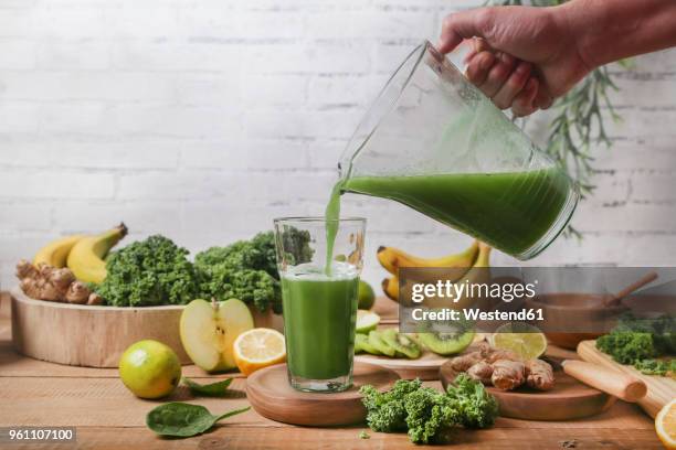 man serving glass of green smoothie surrounded by ingredients - disintossicazione foto e immagini stock