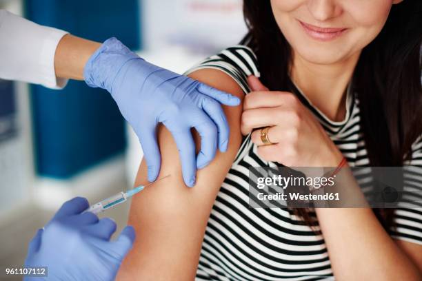 woman receiving an injection in her arm - schots stock-fotos und bilder