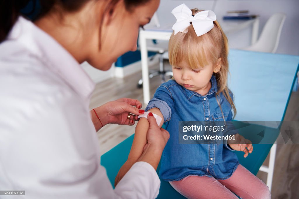 Doctor applying band-aid on girl's arm in medical practice