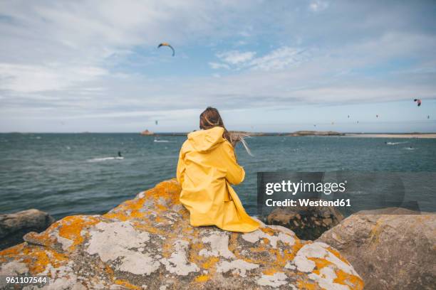 france, brittany, landeda, dunes de sainte-marguerite, young woman sitting on rock at the coast - vêtement de pluie photos et images de collection