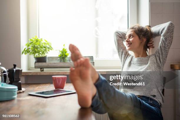 woman sitting at table in kitchen relaxing - feet up 個照片及圖片檔