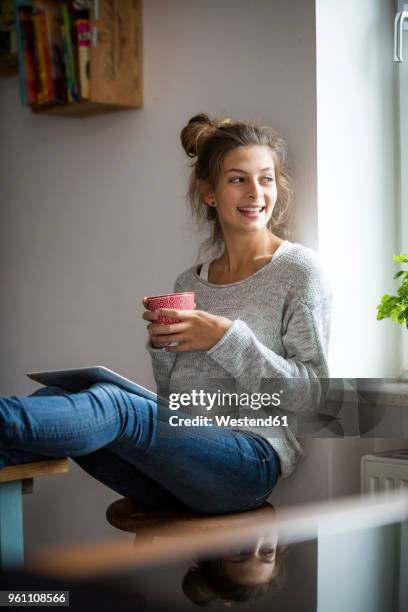 smiling woman sitting on stool with cup and tablet - cup portraits foto e immagini stock