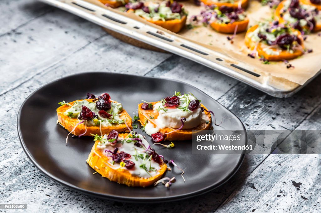 Slices of sweet potato with cream cheese, ramson cream, goat cheese, cress and cranberries