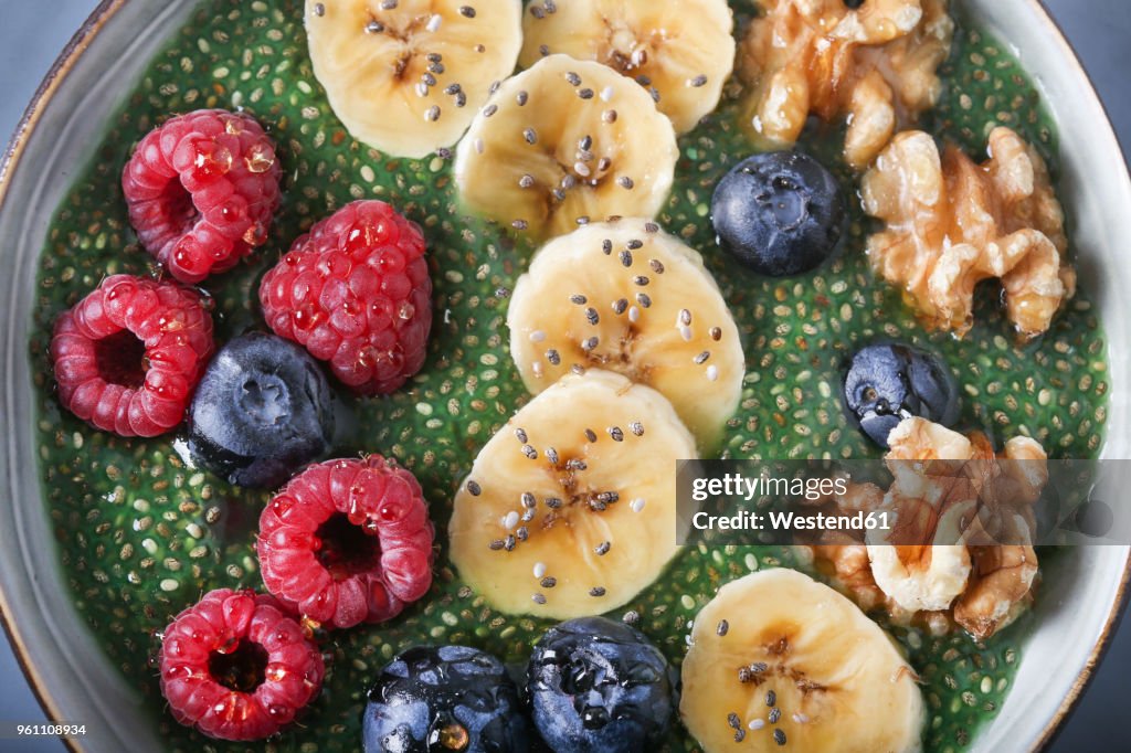 Buddha bowl of green chia pudding with slices of banana, blueberries, raspberries and walnuts