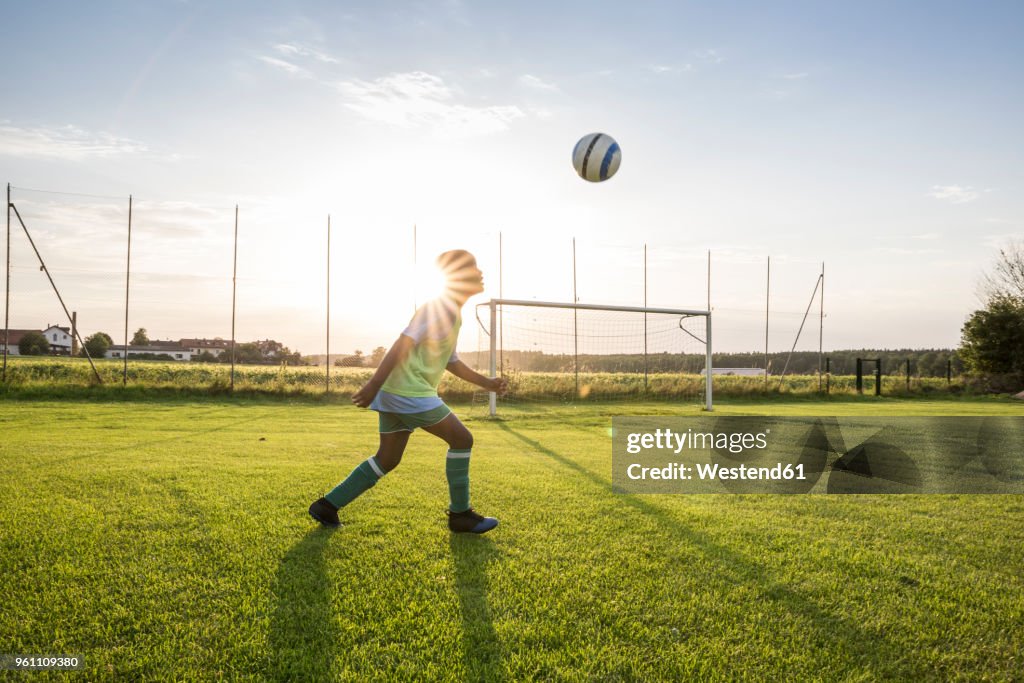 Young football player heading the ball on football ground at sunset