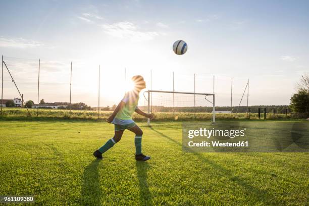 young football player heading the ball on football ground at sunset - heading the ball stock pictures, royalty-free photos & images