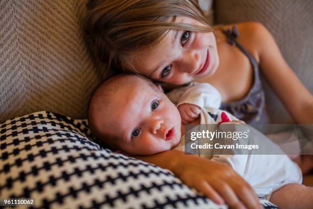 portrait of girl with baby girl lying on sofa at home - hazel bond fotografías e imágenes de stock