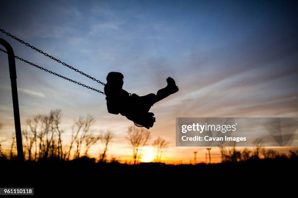 silhouette girl playing on swing against sky during sunset - children playing silhouette stock pictures, royalty-free photos & images