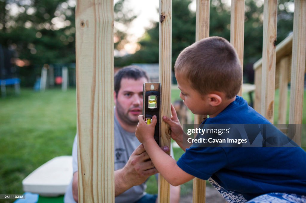 Father teaching son to use spirit level on wooden frame at yard