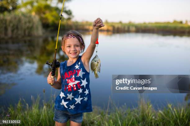 portrait of girl showing off caught fish while standing against lake - fishers indiana stock pictures, royalty-free photos & images