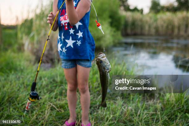 midsection of girl holding caught fish in fishing rod while standing by lake - fishers indiana stock pictures, royalty-free photos & images