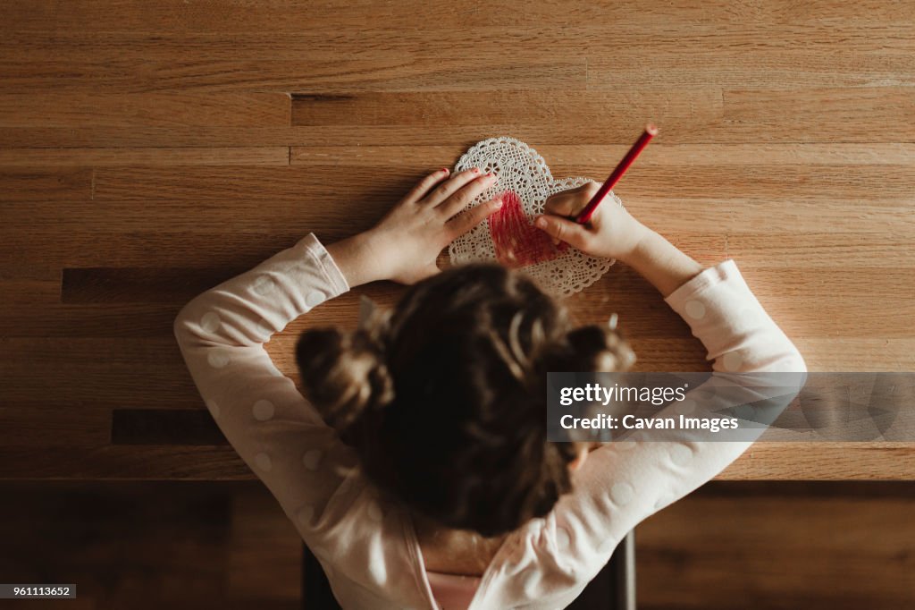 Overhead view of girl making valentine card on table at home