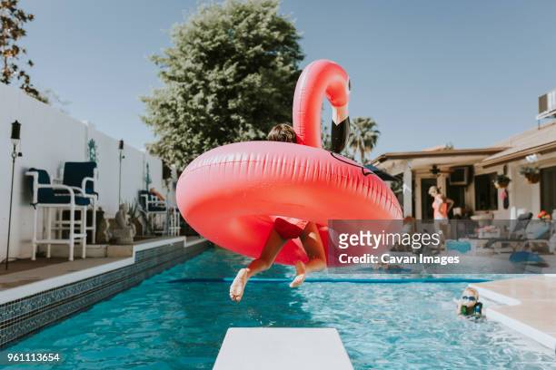 girl jumping into swimming pool with pink flamingo - jump in pool stockfoto's en -beelden