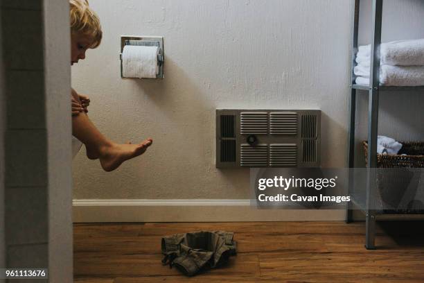 boy looking at pant while sitting on toilet bowl in bathroom - childrens closet stockfoto's en -beelden