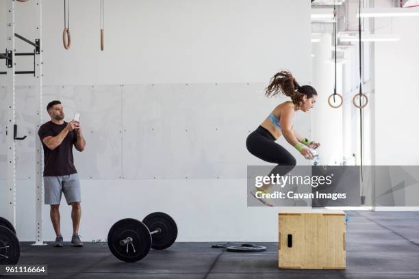 instructor photographing athlete exercising on jump box in gym gym - woman gym boxing stockfoto's en -beelden